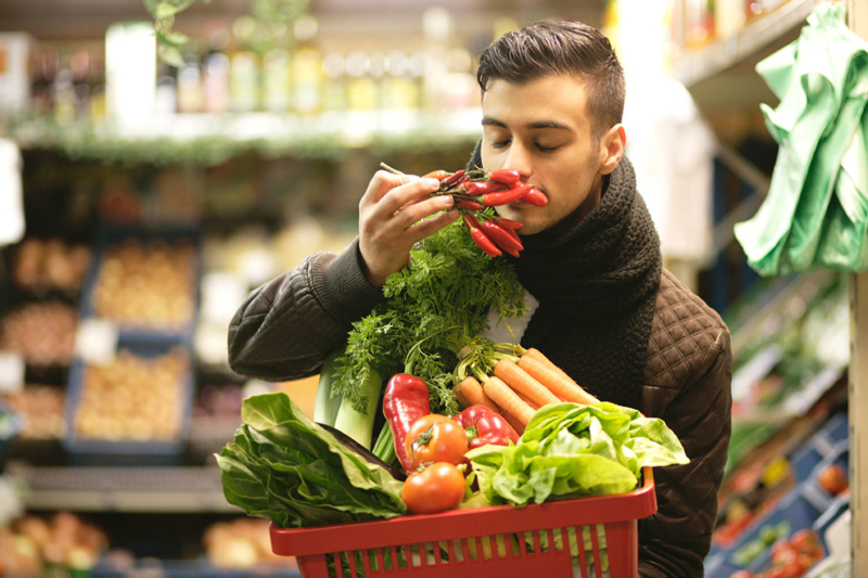 Photo d'un homme faisant ses courses avec un panier remplis de fruits et legumes, homme sent l'odeur de ses legumes, nos collaborateurs peuvent, à travers cette animation, découvrir une manière saine de consommer
