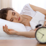 Photo d'une femme dormant tranquillement dans son lit a cote de son reveil, favoriser son endormissement optimise la récupération et est essentiel pour avoir de l'énergie pour une journée au bureau